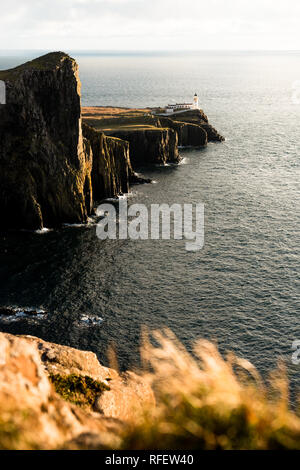 Sonnenuntergang am Neist Point Leuchtturm an der Küste von Skye mit Gras im Vordergrund und sonnigen Himmel (Isle of Skye, Schottland, Vereinigtes Königreich, Europa) Stockfoto