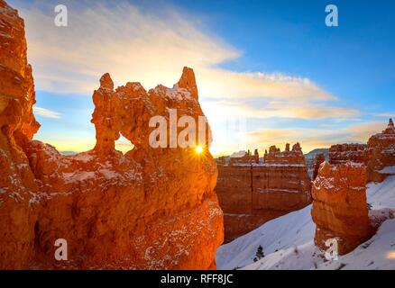 Sun Star glänzt durch die Bohrung in der bizarren Felsformation im Morgenlicht, verschneite Felsen Landschaft mit Hoodoos im Winter Stockfoto