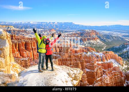 Touristen mit ausgestreckten Armen vor dem Amphitheater, bizarr verschneite felsige Landschaft mit Hoodoos im Winter, Rim Trail Stockfoto