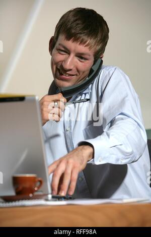 DEU, Deutschland: Junger Mann ist, an seinem Laptop arbeiten, am Telefon Stockfoto