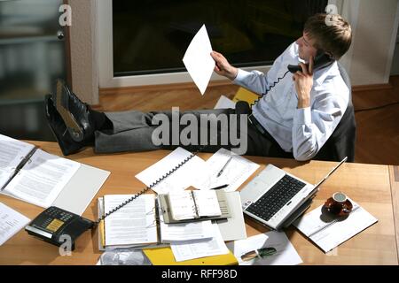 DEU, Deutschland: Junge Mann ist an einem Schreibtisch arbeiten, mit Laptop, auf dem Telefon Stockfoto