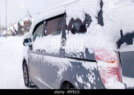 Closeup grau Minibus schmutziges Auto mit Schnee auf der Stadt abgedeckt. Von der Seite. Konzept, Schnee, Schneefall, schlecht nördlichen Wetterbedingungen, niedrig Stockfoto