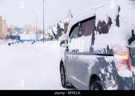 Closeup grau Minibus schmutziges Auto mit Schnee auf der Stadt abgedeckt. Von der Seite. Konzept, Schnee, Schneefall, schlecht nördlichen Wetterbedingungen, niedrig Stockfoto