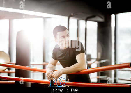 Portrait einer jungen athletischen Mann in Schwarz Sportswear stehend auf dem boxxing Ring an der Turnhalle Stockfoto