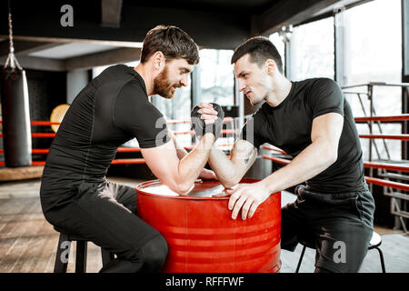 Zwei junge Athleten in schwarz Sportswear eine harte Arm Wrestling Wettbewerb auf einem roten Zylinder in der Turnhalle Stockfoto