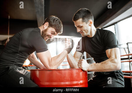 Zwei junge Athleten in schwarz Sportswear eine harte Arm Wrestling Wettbewerb auf einem roten Zylinder in der Turnhalle Stockfoto