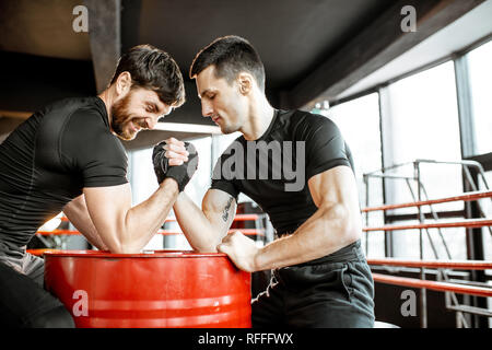 Zwei junge Athleten in schwarz Sportswear eine harte Arm Wrestling Wettbewerb auf einem roten Zylinder in der Turnhalle Stockfoto