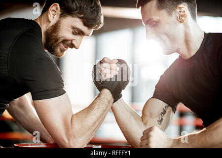 Zwei junge Athleten in schwarz Sportswear eine harte Arm Wrestling Wettbewerb auf einem roten Zylinder in der Turnhalle Stockfoto