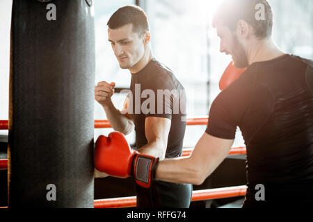 Athletischen Männern in schwarzen Sportswear Training mit Boxsack im Boxring an der Turnhalle Stockfoto