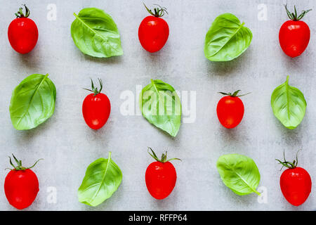 Kreative Gestaltung aus Cherry Tomaten und Basilikum Blätter auf hellen Hintergrund zu schließen. Zutaten für gesundes Kochen. Essen Konzept. Flach, Ansicht von oben Stockfoto