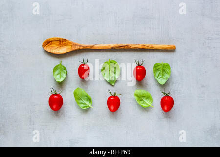 Gesundes Kochen Zutaten flach. Kreative Gestaltung aus Holzlöffel, Cherry Tomaten und Basilikum Blätter auf hellen Hintergrund. Essen Konzept. Ansicht von oben Stockfoto