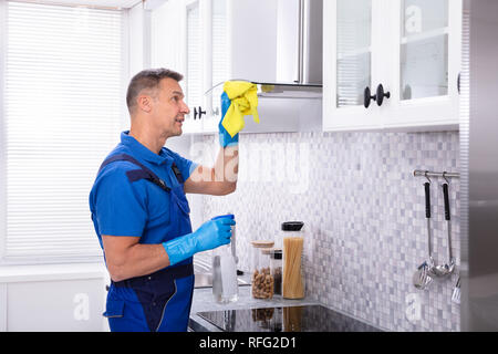 Reife männliche Hausmeister Reinigung Dunstabzugshaube mit Serviette und Spray Waschmittel in der Küche Stockfoto