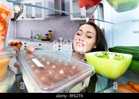 Nahaufnahme einer Lächelnden jungen Frau unter Nachtisch vom Kühlschrank Stockfoto