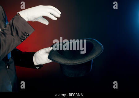 Berufliche Tätigkeit. Showman in Anzug und Handschuhe auf Wand, Tricks mit Hut in der Nähe isoliert aufstehen Stockfoto
