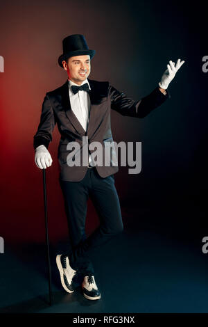 Berufliche Tätigkeit. Showman, Handschuhe und Hut stehen auf Wand mit Zuckerrohr posiert verspielt lächelt Fröhlich voller Körper geschossen isoliert Stockfoto