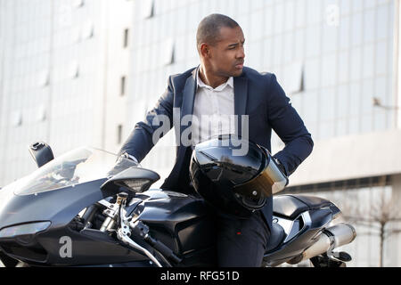 Junger Mann sitzen auf dem Motorrad mit Helm zurück schauen nachdenklich Stockfoto