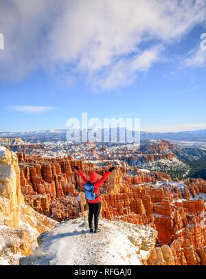 Junge Frau mit ausgestreckten Armen, mit Blick auf das Amphitheater, bizarr verschneite felsige Landschaft mit Hoodoos im Winter, Rim Trail Stockfoto