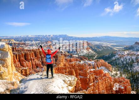 Junge Frau mit ausgestreckten Armen und Blick auf das Amphitheater, bizarr verschneite felsige Landschaft mit Hoodoos im Winter Stockfoto