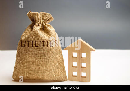 Eine Geld-Beutel mit dem Wort Dienstprogramme und ein Holzhaus. Das Konzept, um das Geld für die Bezahlung der Dienstprogramme. Die Anhäufung von Geld. Ein großes d Stockfoto