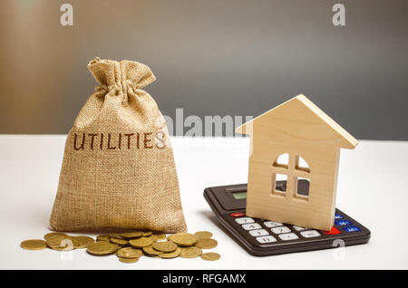 Eine Geld-Beutel mit dem Wort Dienstprogramme und ein Holzhaus. Das Konzept, um das Geld für die Bezahlung der Dienstprogramme. Die Anhäufung von Geld. Ein großes d Stockfoto