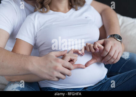 Nahaufnahme der schwangeren Frau mit Mann hält ihre Hände auf Ihren geschwollenen Bauch Gestaltung ein Herz Stockfoto