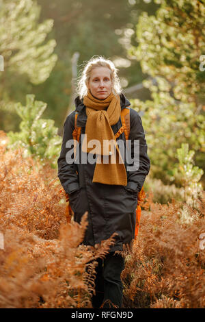 Eine Frau, die zu Fuß in einem Wald mit vielen orange Farne