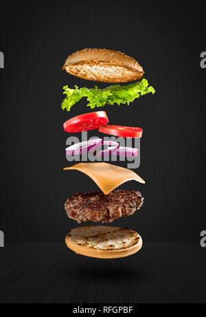 Lecker Hamburger mit fliegenden Zutaten auf schwarzem Hintergrund Stockfoto