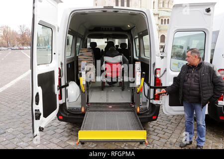 Sofia, Bulgarien - 7. Januar 2019: Treiber unterstützt einen körperlich behinderten Mann im Rollstuhl, der in einem Minibus mit Rollstuhlrampe verstaut zu erhalten. Stockfoto