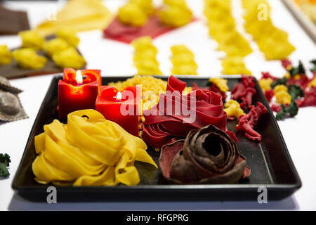 Verschiedene Arten von italienischer Pasta. Verschiedene Farben von Nudeln in Platten mit Kerzen gesehen von oben. Stockfoto