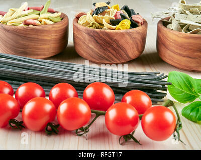 Trockenteigwaren: Bunte orechiette, Fusilli, Tagliatelle, Spaghetti, frische Tomaten und Basilikum, auf einem Holzbrett Stockfoto