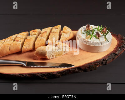 Gebackener Camembert mit Walnüssen, Rosmarin Stängel und Knoblauchzehen, serviert mit knusprigem Knoblauch große, auf einem urigen Board Stockfoto