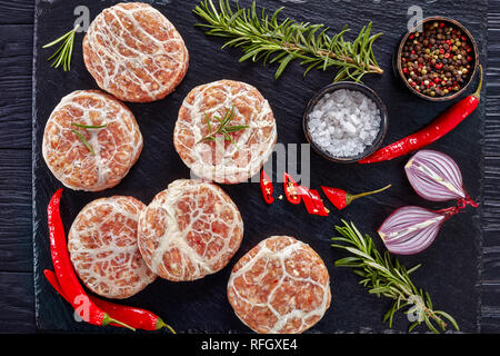 Ungekocht Atriaux - Schweinefleisch in caul Fett gewickelt, Schweizer Küche, Art der Bratwurst auf einer Schiefertafel Fach mit Zwiebel, Rosmarin, Pfeffer und Salz, auf einer Stockfoto