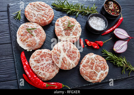 Raw Atriaux - Schweinefleisch in caul Fett gewickelt, Schweizer Küche, Art der Bratwurst, Hamburger auf einer Schiefertafel Fach mit Zwiebel, Rosmarin, Pfeffer und Salz, o Stockfoto