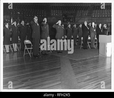 Schwarz-weiß Foto, innen ein Auditorium mit mehreren Sitzgelegenheiten Ebenen getroffen, einer Gruppe von Männern und Frauen, die uns militärische Uniformen und Anheben der rechten Hand auf ihre Stirn in Salute, mit vier mehr Männer am Recht, das Tragen ziviler Kleidung, mit der rechten Hand über ihre Herzen, mit Fahnen und eine Band in der ganz linken Hintergrund sichtbar, während des Vietnam Krieges, 1967 fotografiert. () Stockfoto