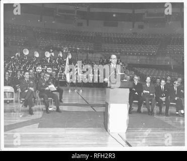 Schwarz-weiß Foto, innen ein Auditorium mit mehreren Sitzgelegenheiten Ebenen getroffen, einer mittleren Alters, spectacled Mann, das Tragen einer Uniform, sprechen von einem zentralen Podium, mit Brigadegeneral Frank L Gunn (mit gekreuzten Arme und Beine) sitzt auf einem Klappstuhl am linken Mittelgrund, neben Ein uniformierter Mann, der durch Papiere aussieht, mit vier Männern das Tragen ziviler Kleidung sitzen auf der rechten Seite und mit Fahnen und sitzt Bandmitglieder im Hintergrund sichtbar, während des Vietnam Krieges, 1967 fotografiert. () Stockfoto