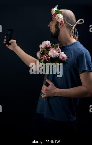 Männliche Blüten tragen, Haarband und halten einen Blumenstrauß ist selbst ein selfie. Romanische Geschenk für den Valentinstag Stockfoto