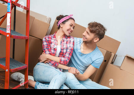 Young couple moving to new place sitting hugging holding hands smiling joyful Stockfoto