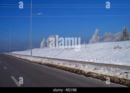 Snowy Damm neben einer Autobahn an einem kalten sonnigen blauen Himmel Winter mit Schnee bedeckten Bäumen o die Skyline in einem Wetter und Jahreszeiten Konzept Stockfoto