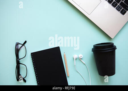 Arbeitsbereich in einem trendigen Blau. Viele verschiedene Dinge wie einen Laptop und Kopfhörer sind auf dem Tisch. Stockfoto