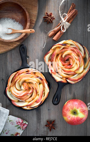 Hausgemachte Blätterteig mit Rose geformte Apfelspalten gebacken in Eisen skillets. Top lag auf Holzbrett mit einigen Äpfeln und Zucker Stockfoto