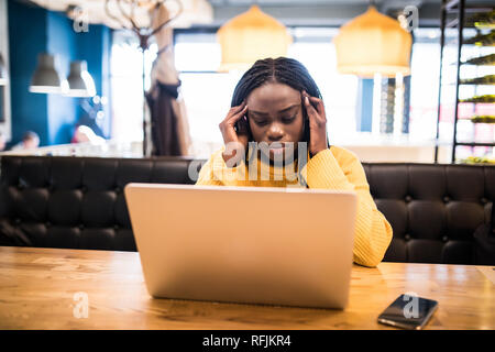 Junge Frau mit Kopfschmerzen während auf Laptop im Cafe arbeiten Stockfoto