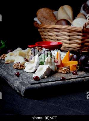 Käseplatte mit Trauben, Honig, Nüsse und Brot Korb auf einem Holz- Hintergrund. Verschiedene Arten von Käse Stockfoto