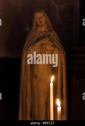Zwei Kerzen leuchten. Im Hintergrund, die Statue der Jungfrau Maria Christus an das Kreuz. Stockfoto