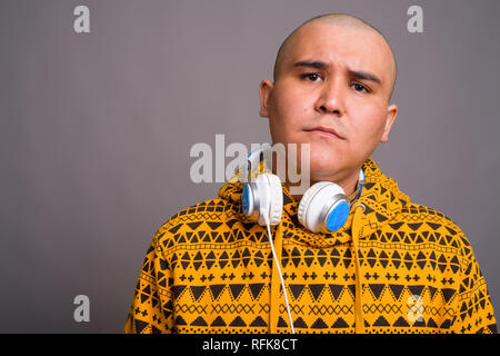 Junge kahle asiatischer Mann mit Kopfhörern gegen grauer Hintergrund Stockfoto