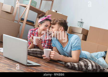 Junges Paar nach New liegend mit Laptop holding Tassen für Tee an jedem anderen spielerischen Nähe suchen Stockfoto