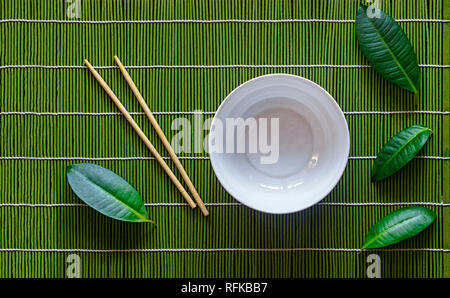 Leeren sack Schüssel, japanisch Tabelle Einstellung mit tropischen Blättern. Bambus Matte, Essstäbchen Stockfoto
