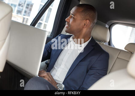 Junge Unternehmer sitzen auf der Rückbank im Auto Arbeiten am Laptop, die man vom Fenster aus sieht nachdenklich Stockfoto