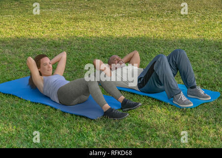Sie beginnen, indem Sie situps auf Yoga Matten auf dem Gras, als Teil der Übung Routine. Gesundes Leben ist wichtig, um eine moderne Paar. Stockfoto
