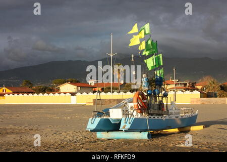 Grüne Boot mit Fahnen von der Sonne beschienen. Immigranten am Strand gelandet sind. Die bunten Boot am Strand gestrandet Stockfoto