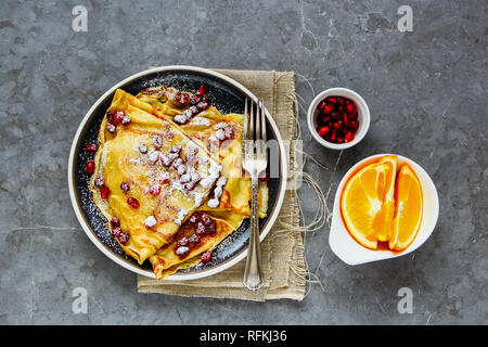 Hausgemachte Crepes gefüllt mit Granatapfel und Zucker in der Platte. Flachbild-lay von dünnen Pfannkuchen und Früchte Stockfoto